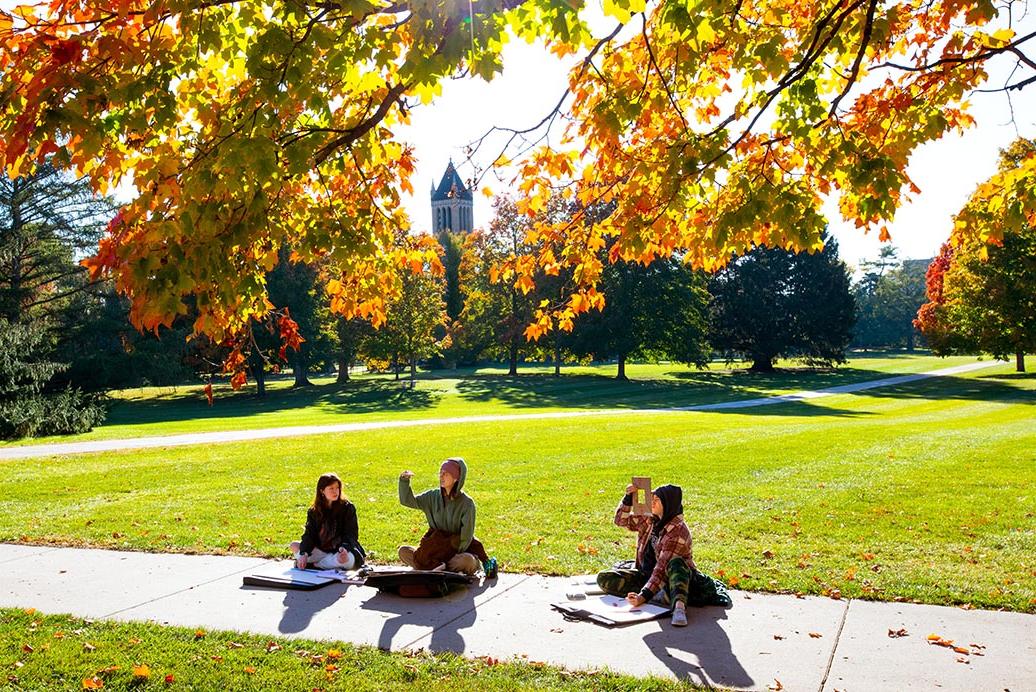 在一个阳光明媚的秋日，三名学生坐在校园中心做一个项目.